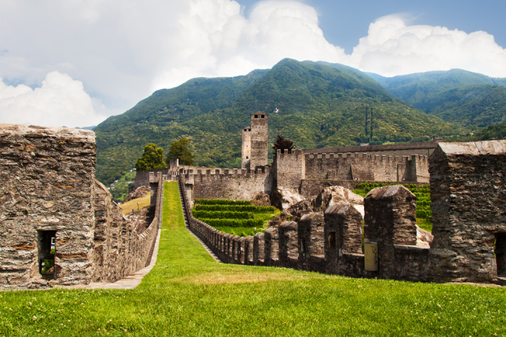 Stone castle and walls with mountains and blue sky in the background.