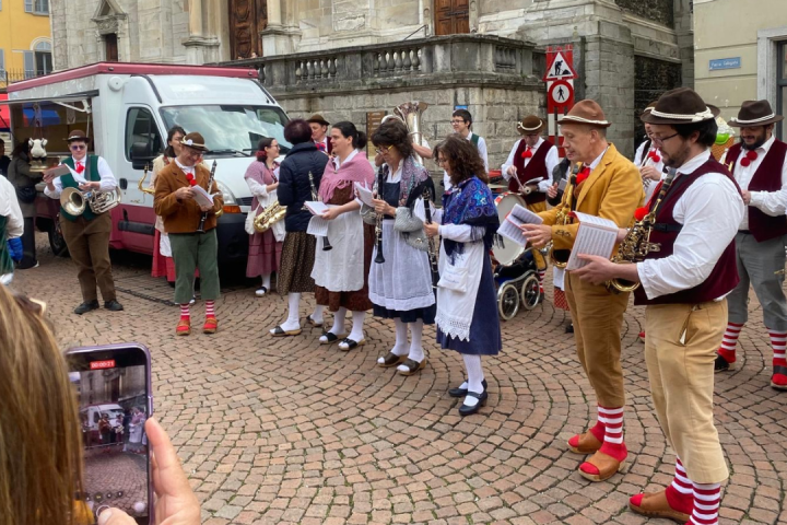 Group in traditional costumes playing instruments in a cobblestone street, with a food truck nearby.