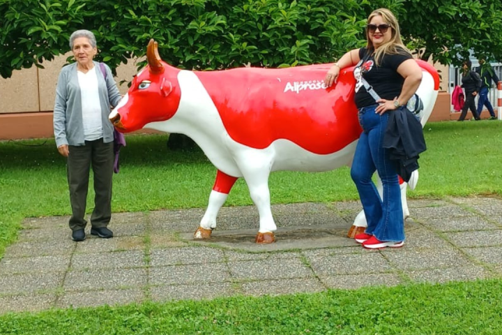 Two people posing with a red and white cow sculpture in a park.