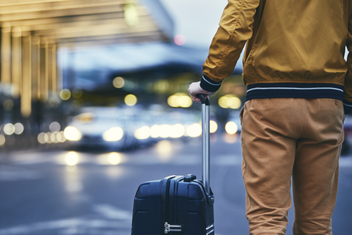 Person with suitcase standing near cars in a city at night.