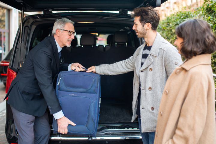 Man helping couple load luggage into black van on city street.
